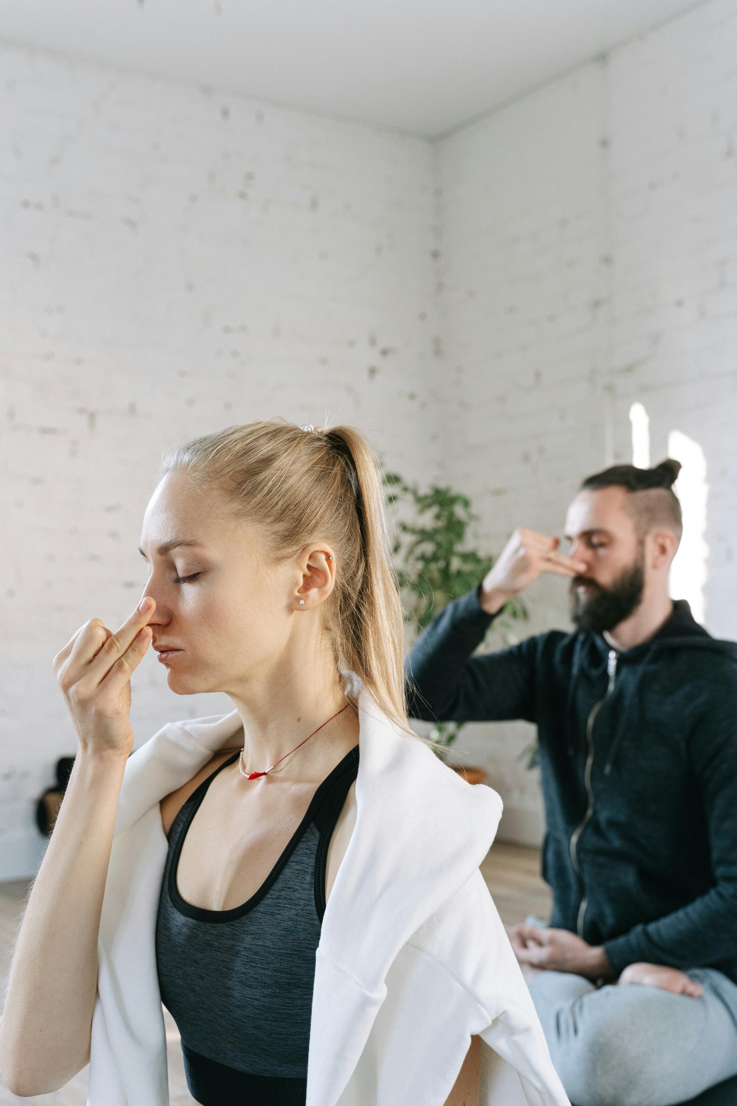 A man and woman sitting in a Breathwork session in a meditation pose cross legged with fingers on the one side of their nose breathing in through the other