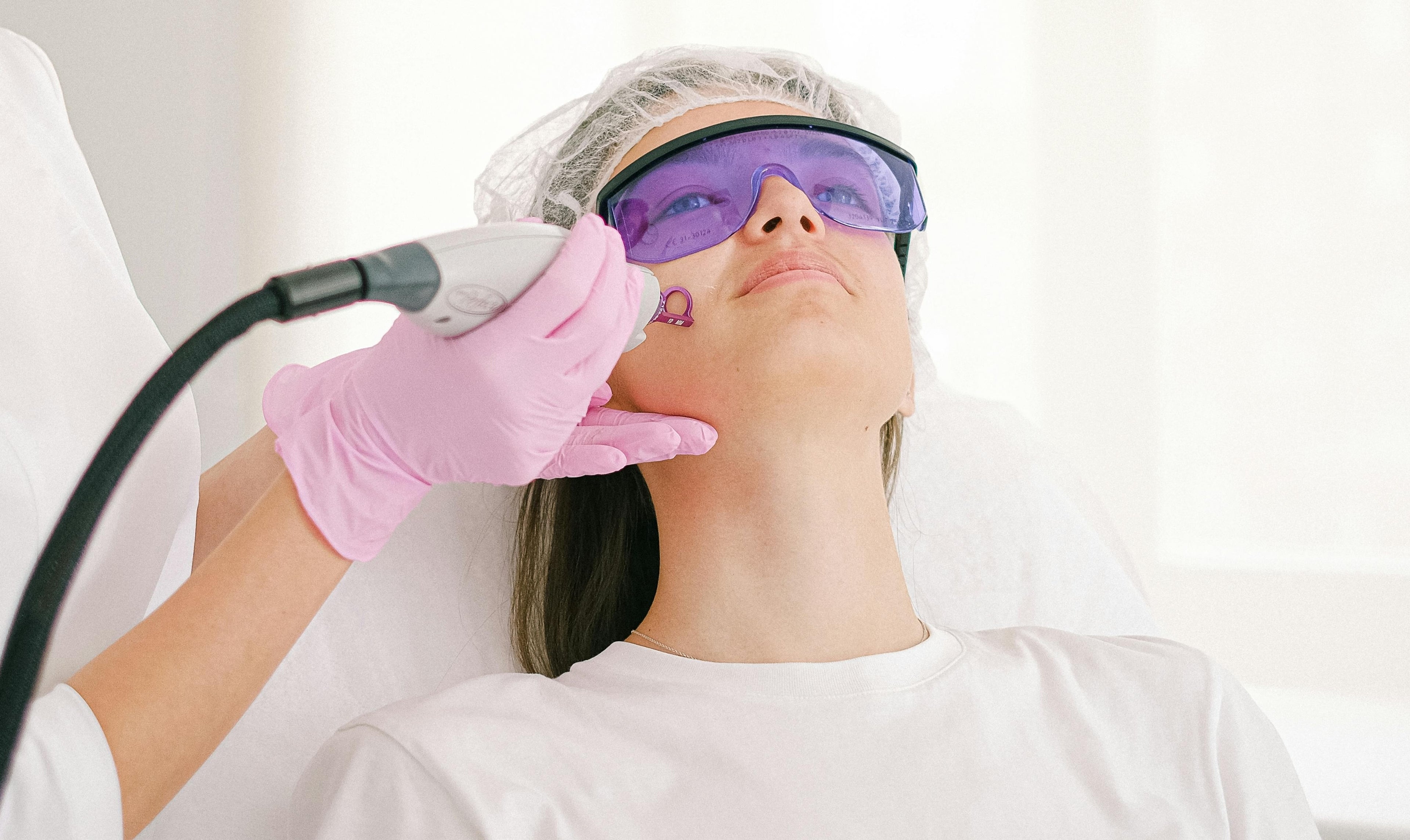 Person receiving a laser treatment on their face with protective eyewear and gloves.