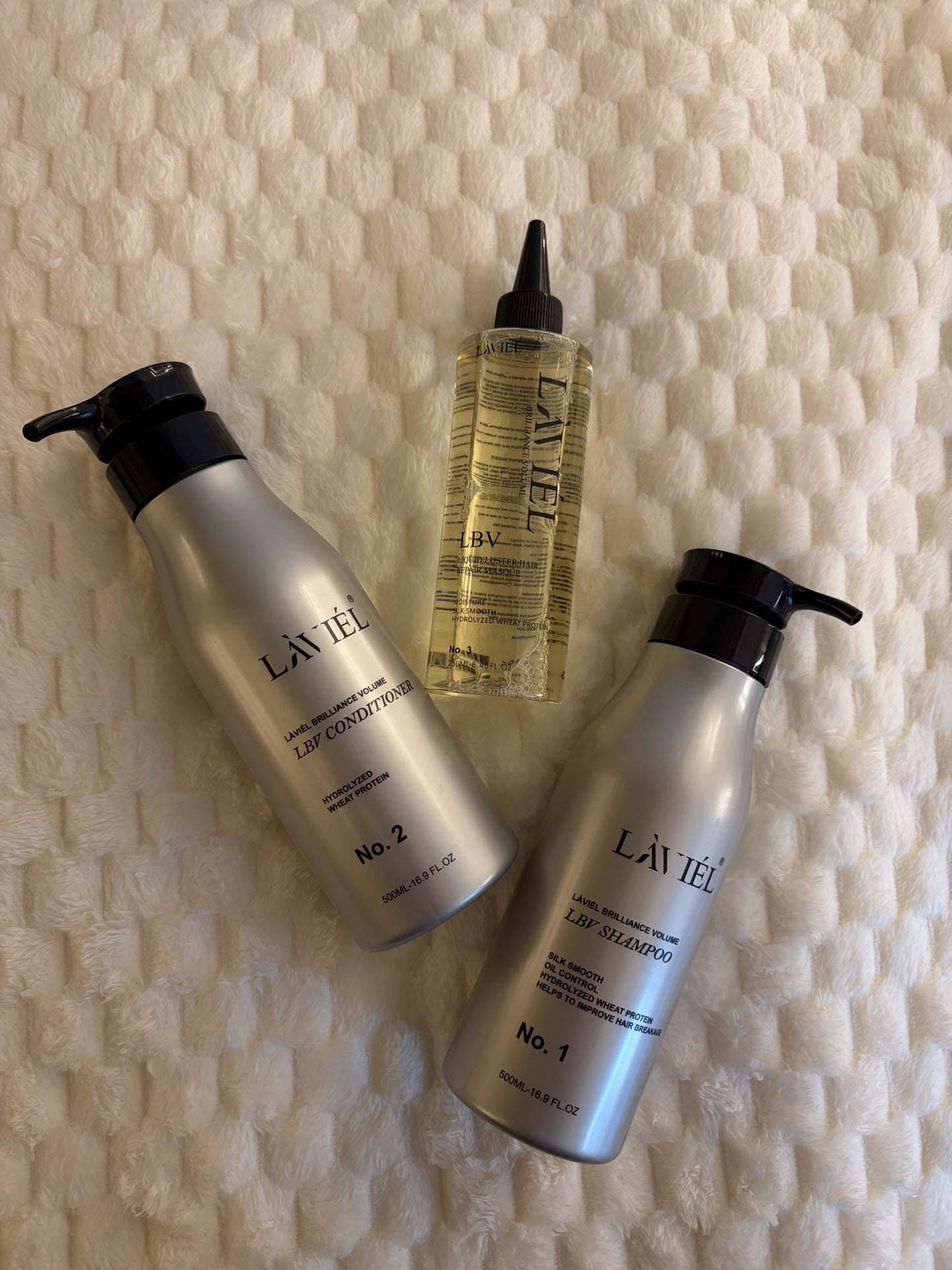 Three bottles of LáVieL hair care products on a textured beige background