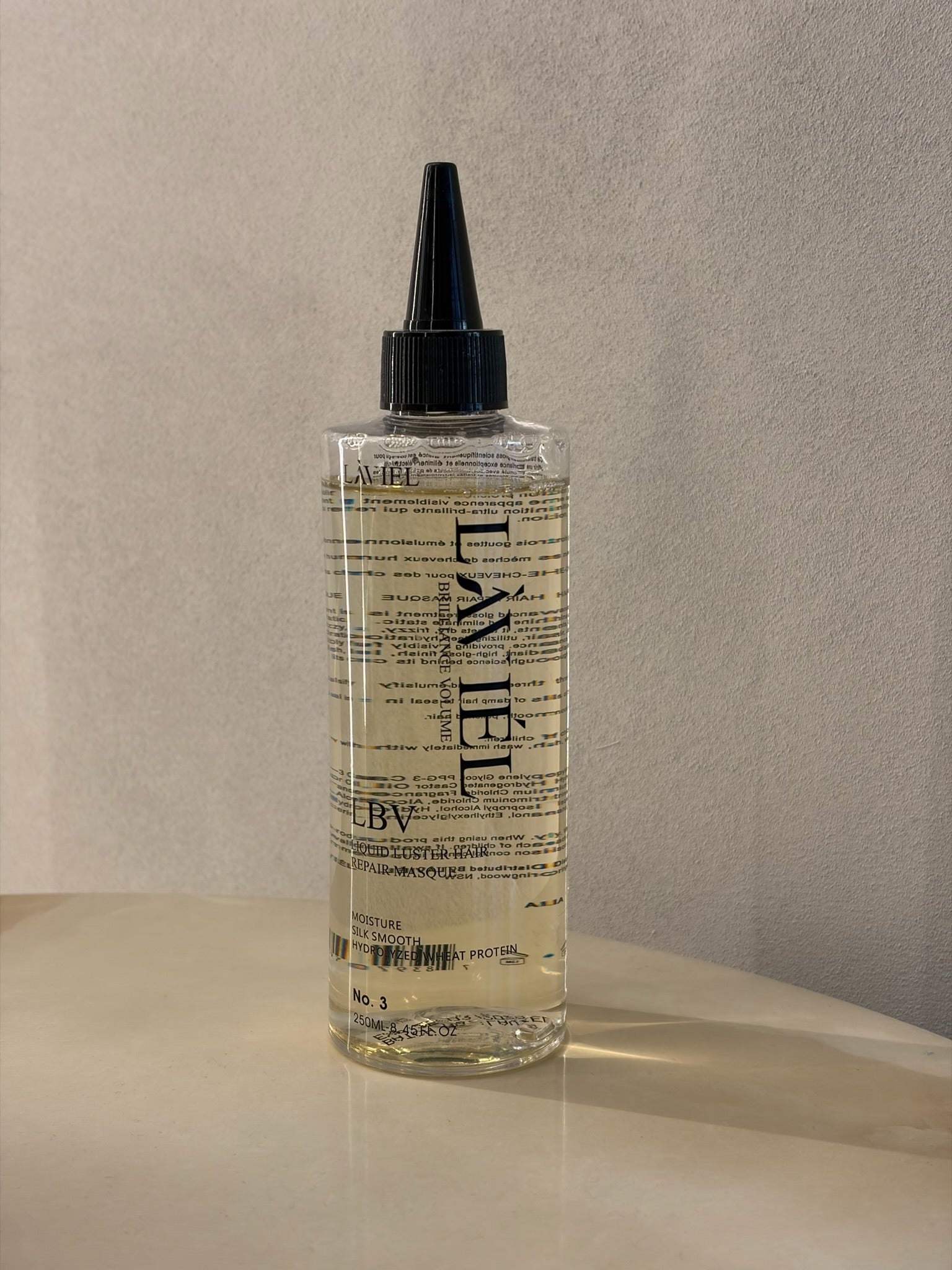 Bottle of L'AVEL hair product on a beige surface with a neutral background