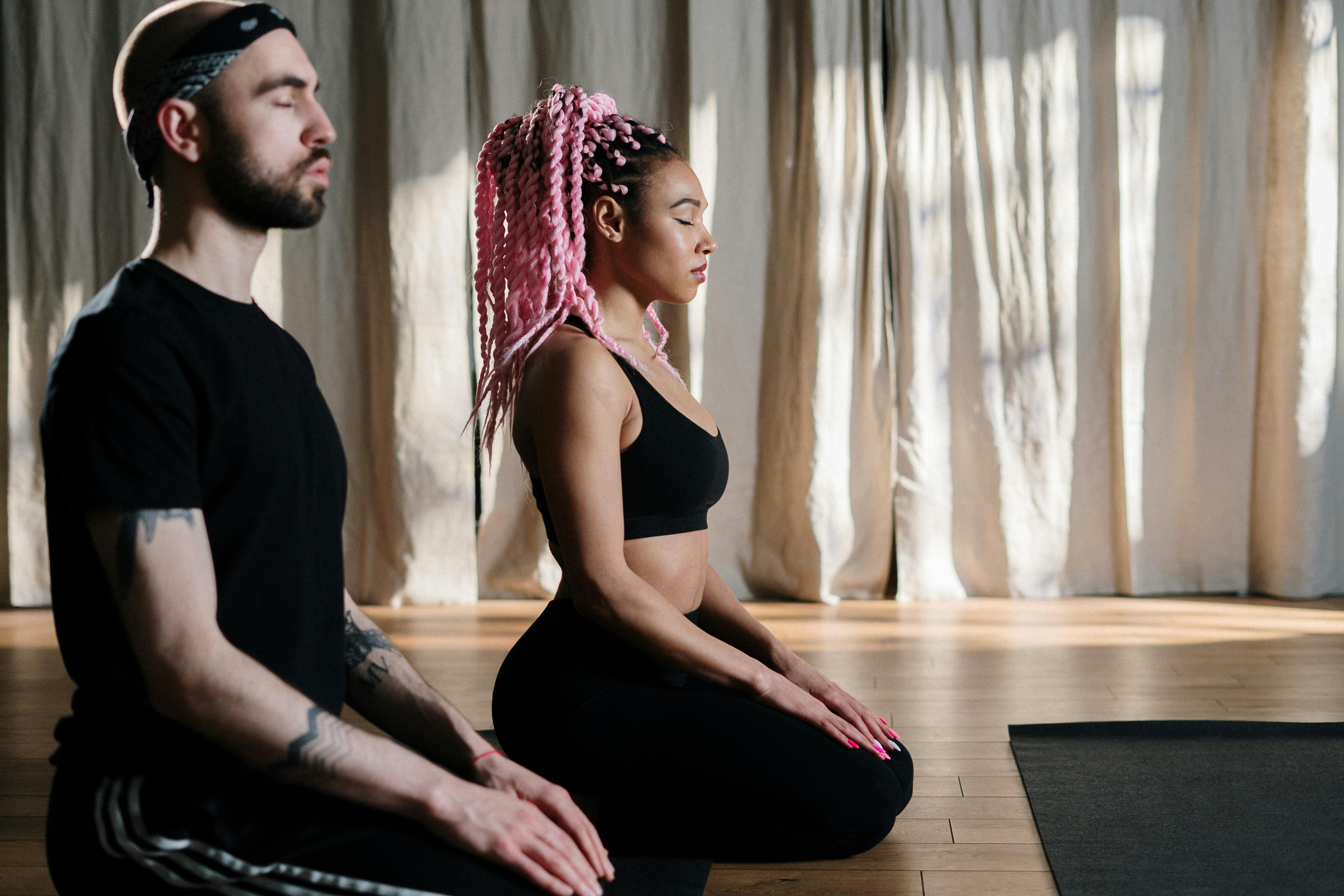 A woman and a man in meditative position meditating in a dimly lit studio
