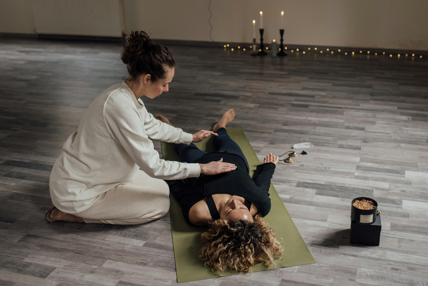 A Reiki practitioner, placing her hands on a Reiki receiver laying down on a mat